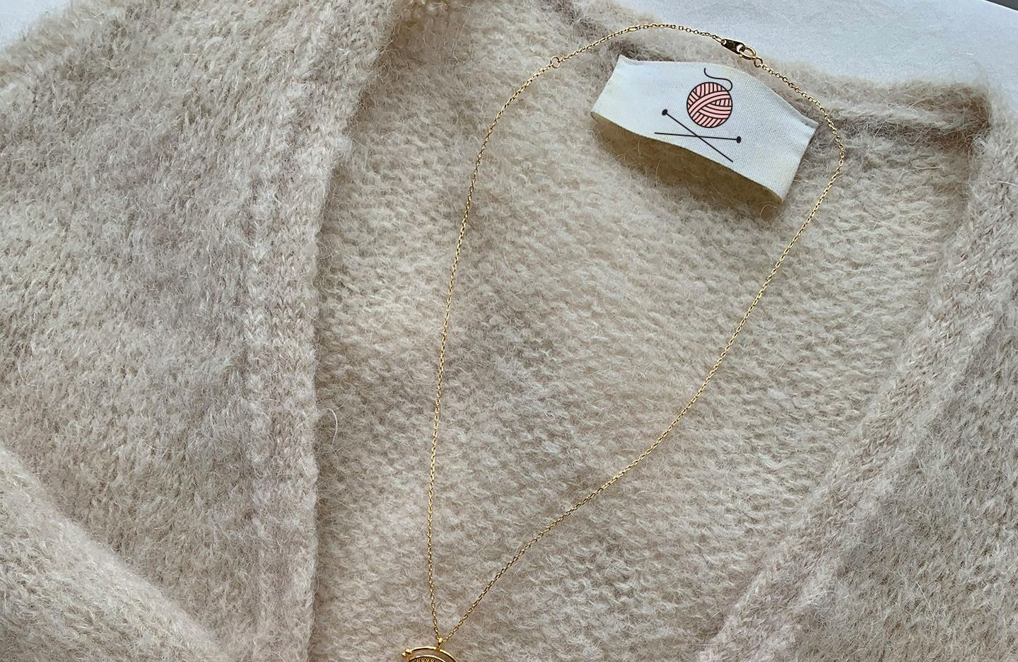 Cream-colored fuzzy cardigan with gold necklace; Killin' Knit garment tag visible.