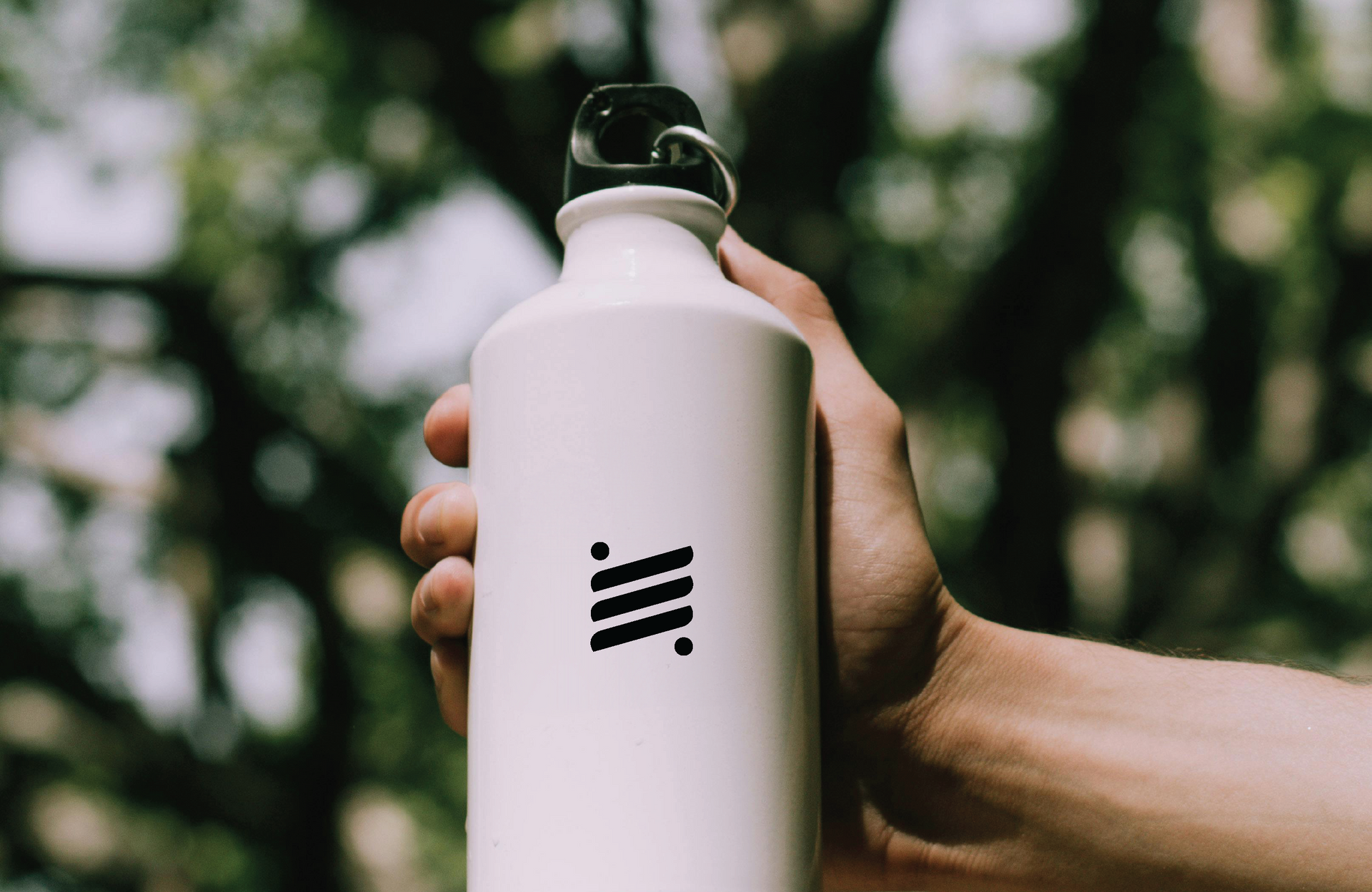 Hand holding a white water bottle with a black Scout logo, against a blurred green background.