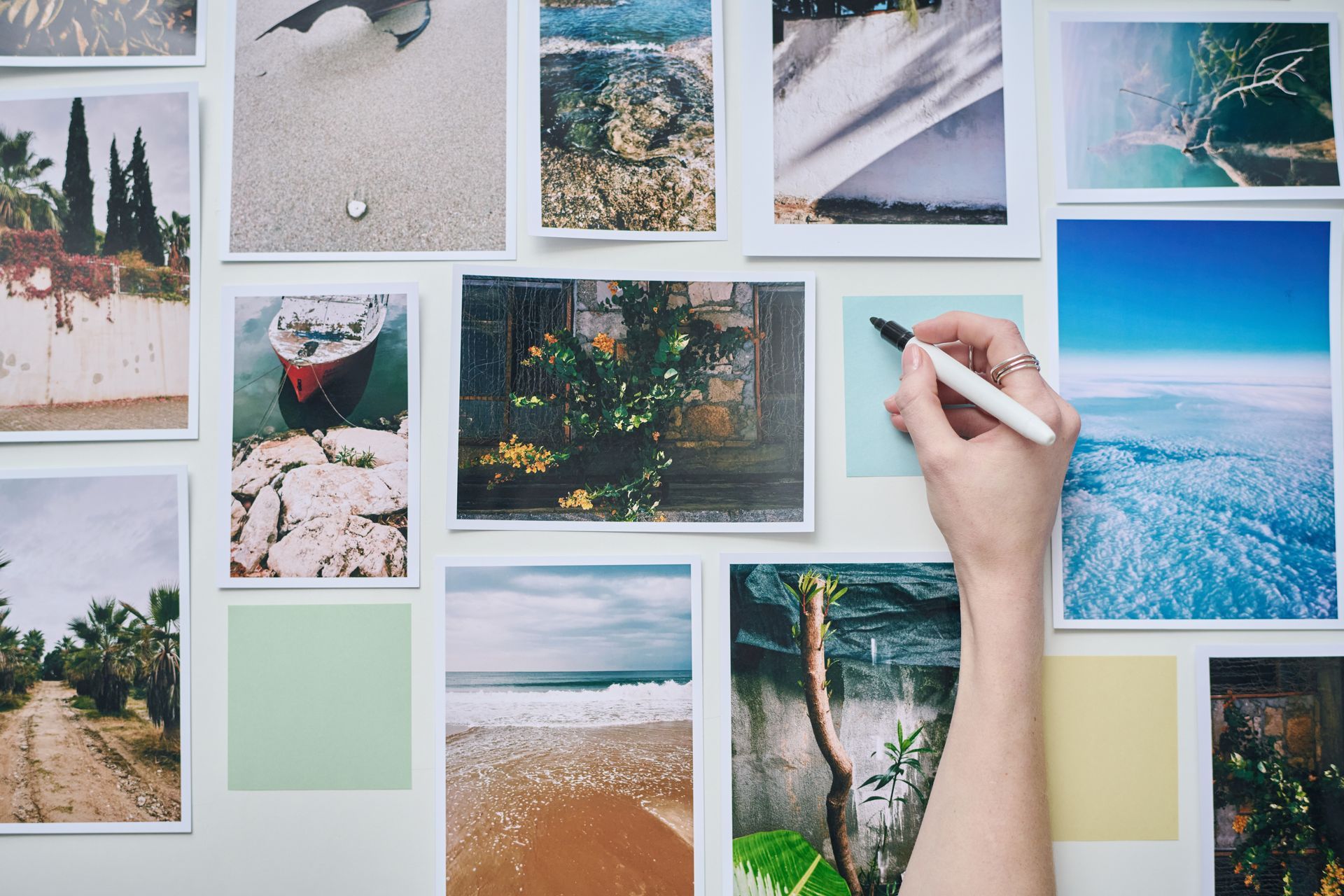 Hand writing on a light green sticky note on a wall with various printed photos.