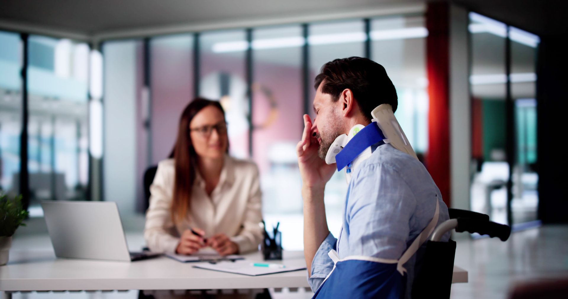 Injured client in a neck brace and wheelchair consulting with an attorney