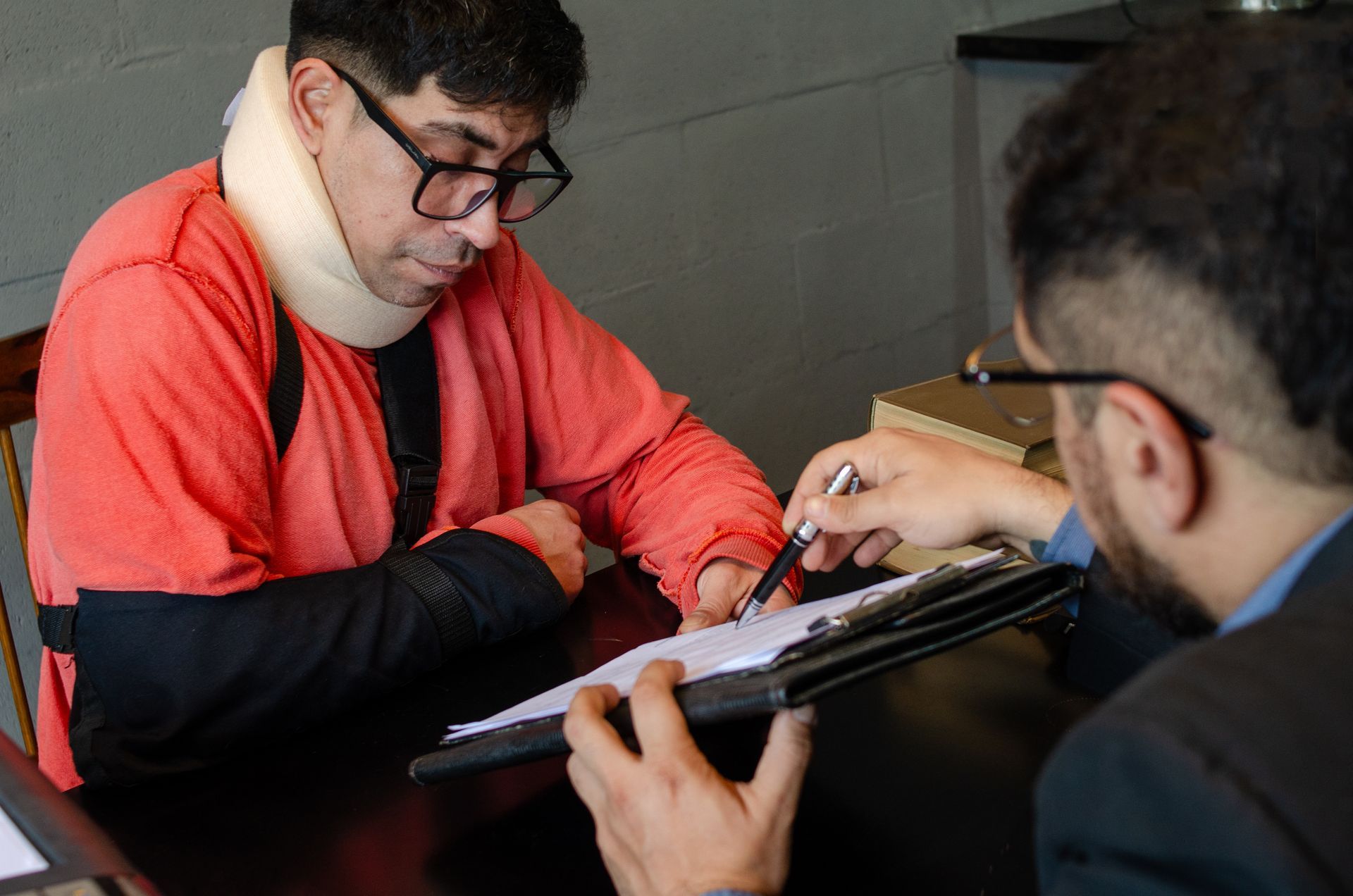 Injured client in a neck brace signing legal documents with an attorney