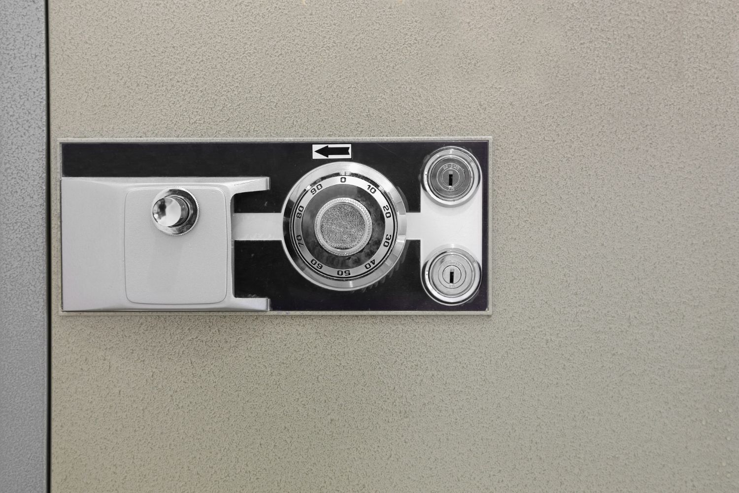 Safe lock with combination dial and keyholes on a textured wall.