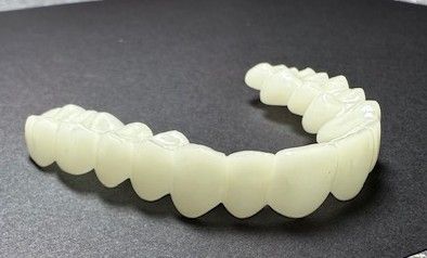 A dental veneer in an arc shape, made of off-white plastic.