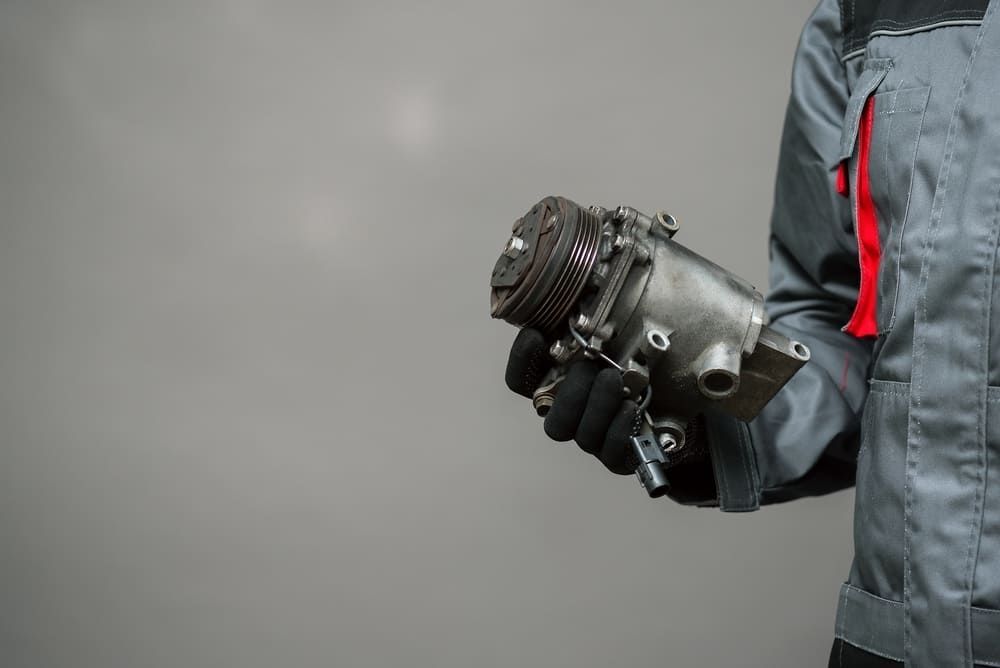 A Man Is Holding A Compressor In His Hands — Twin City Auto Dismantlers In Corowa, NSW