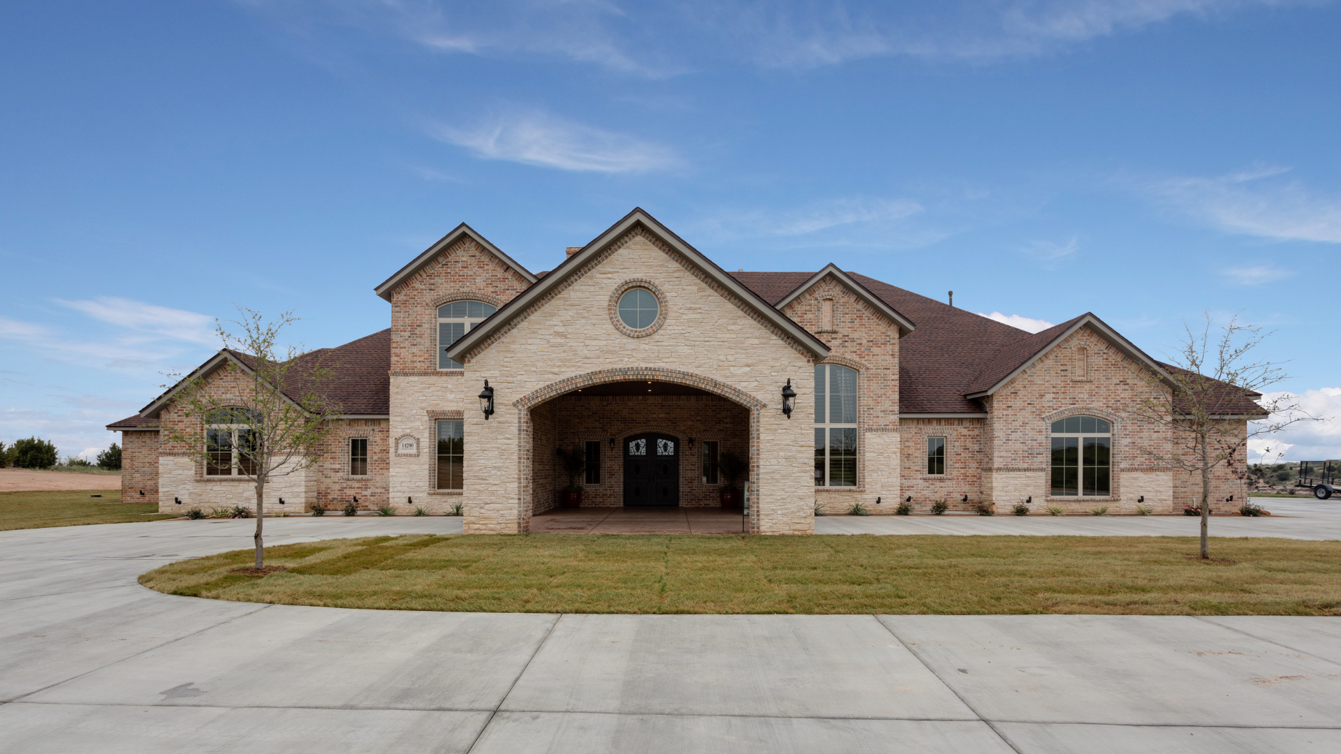 Large stone house with a warm-lit entrance, curved driveway, and lush green lawn at sunset