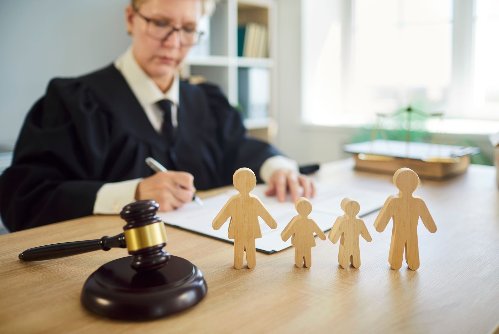 Judge with gavel beside wooden family figures on a desk in a courtroom setting Judge with gavel beside wooden family figures on a desk in a courtroom setting