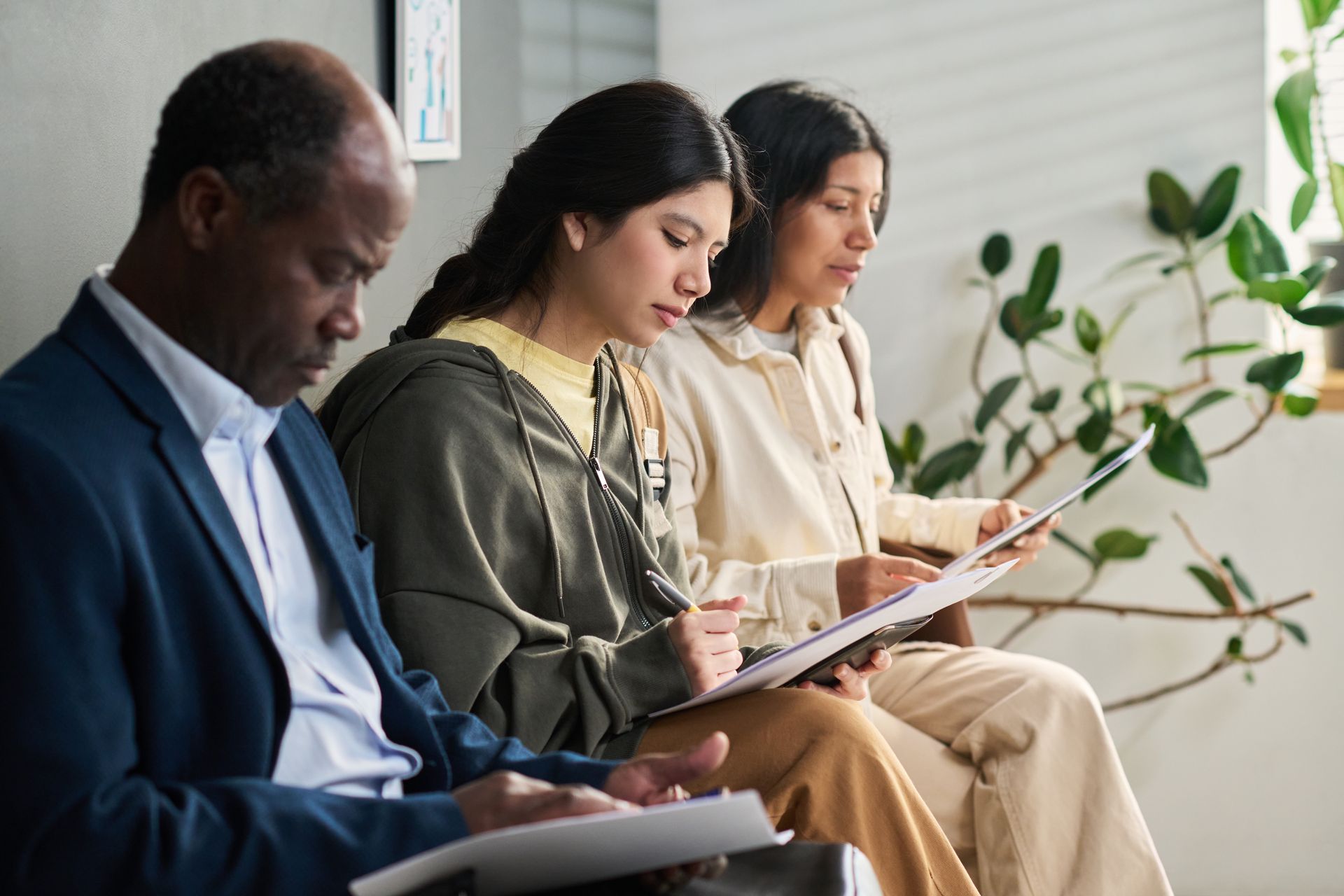 Three people seated in a bright office, reading papers during a meeting.