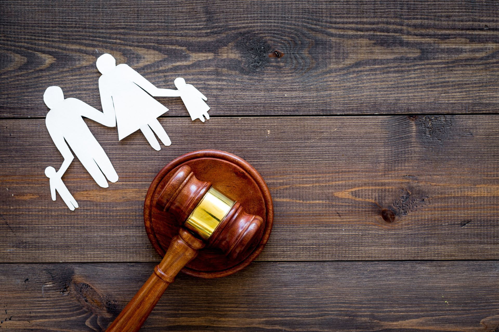Judge’s gavel beside white family cutouts on a wooden table Judge’s gavel beside white family cutouts on a wooden table