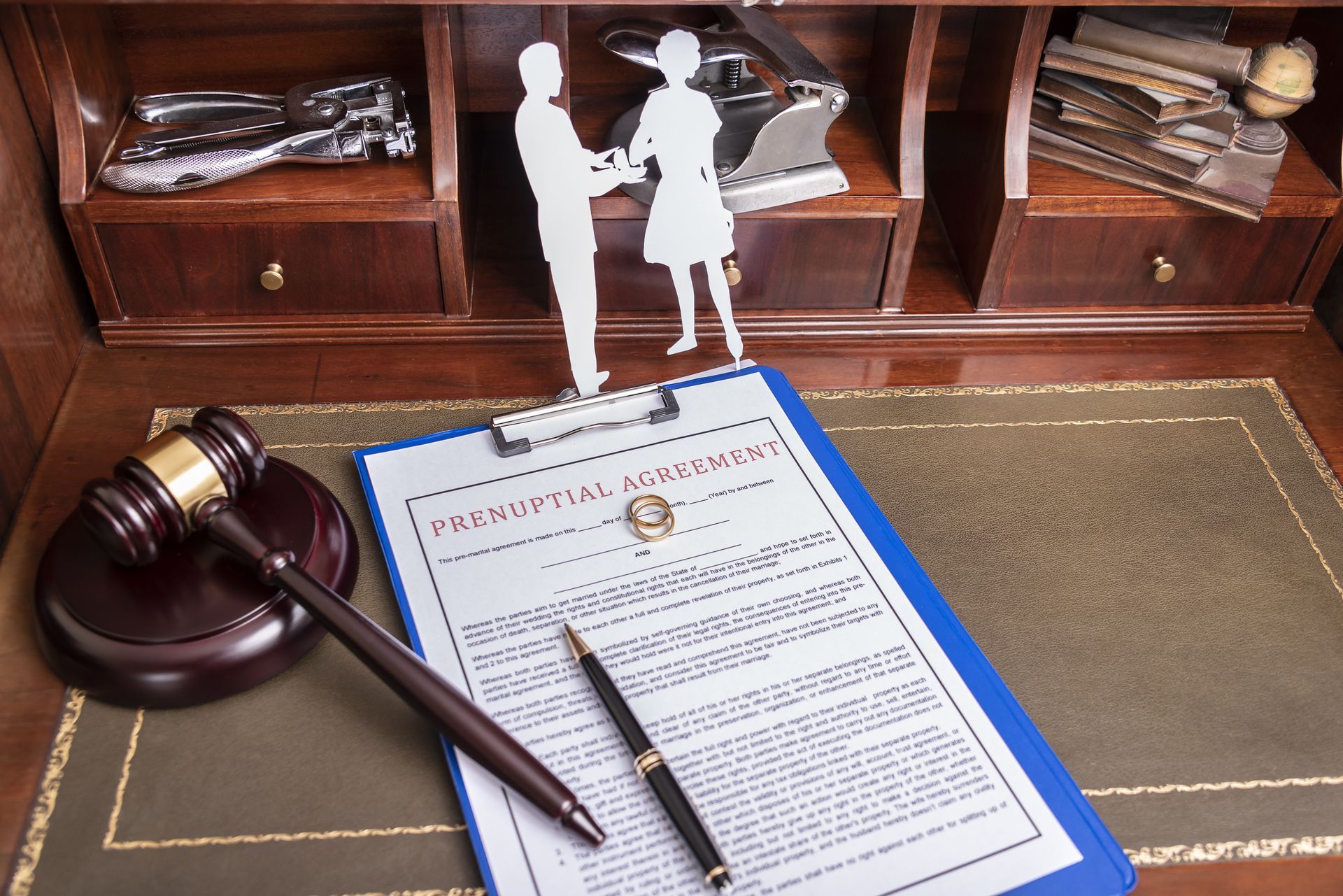Gavel and pen beside a blue-bordered document on a desk in a law office with shelves and figurines. Gavel and pen beside a blue-bordered document on a desk in a law office with shelves and figurines.