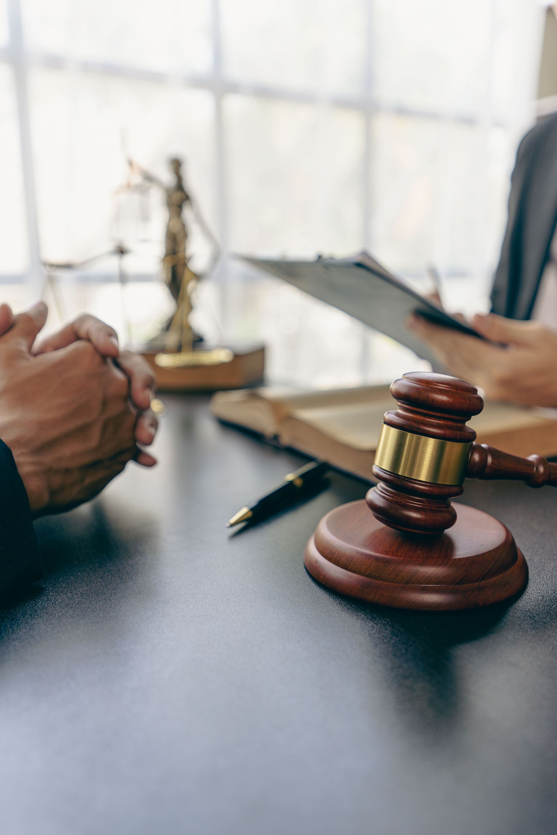 Judge’s gavel on a desk in a courtroom, with people discussing documents in the background.
