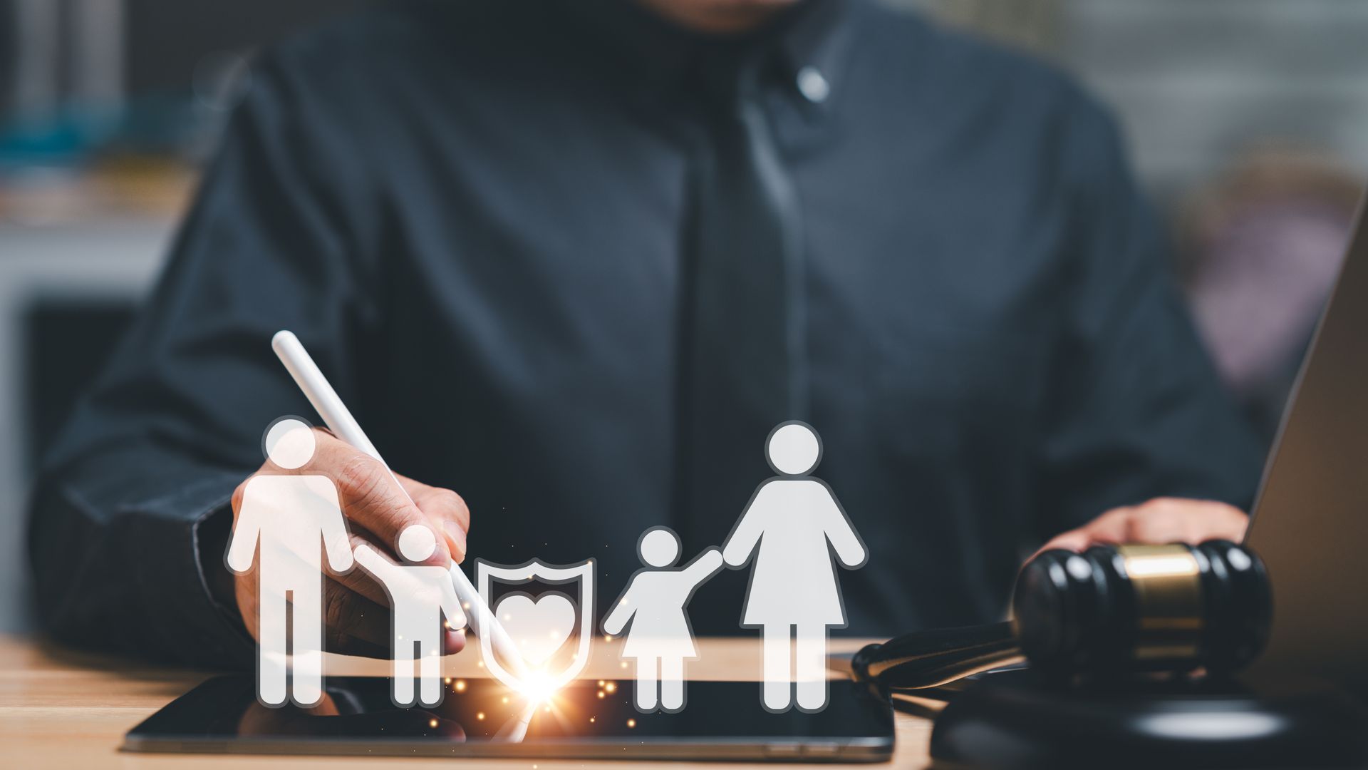 Person pointing at glowing family icons on a tablet with a stylus, near a gavel