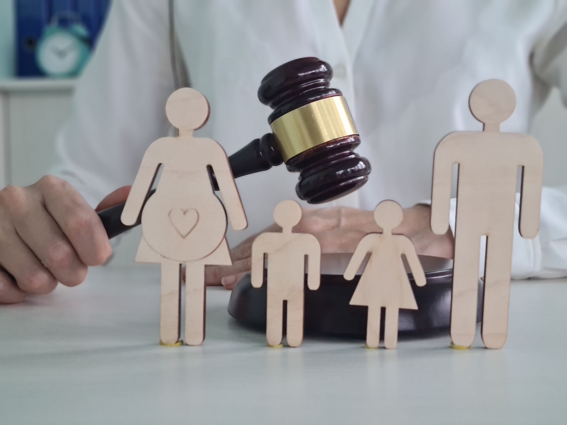 Wooden family figures before a judge’s gavel, suggesting family law or custody decision.