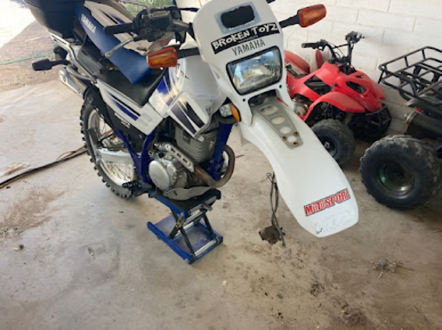 Blue Yamaha dual-sport motorcycle parked indoors beside a red ATV, front wheel on a stand.