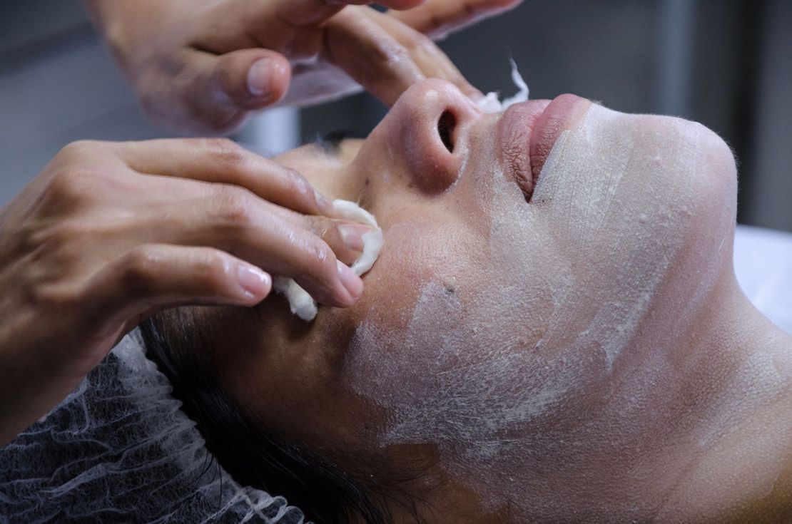 Primer plano de una persona recibiendo un tratamiento facial espumoso en una camilla de spa.