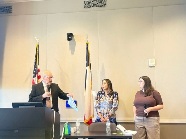 Vanessa and two presenters stand at the front of a room.