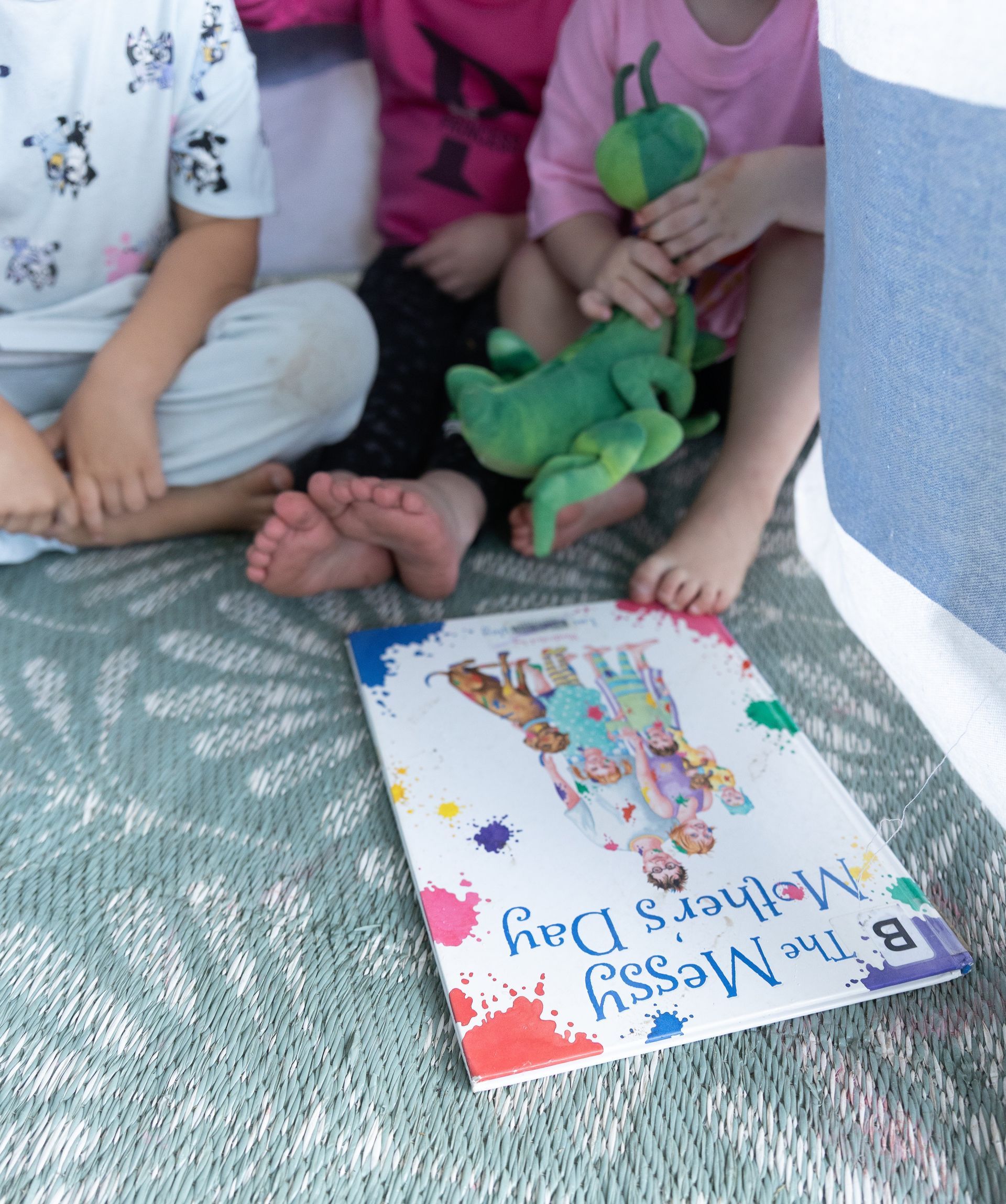 Children sitting on a mat with a green toy and a colorful book on the floor