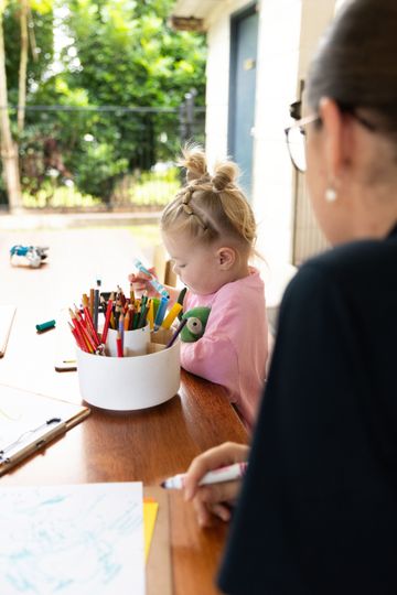Adult and child drawing at a table with colorful pencils outdoors
