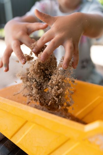Hands sifting soil into a yellow bin outdoors