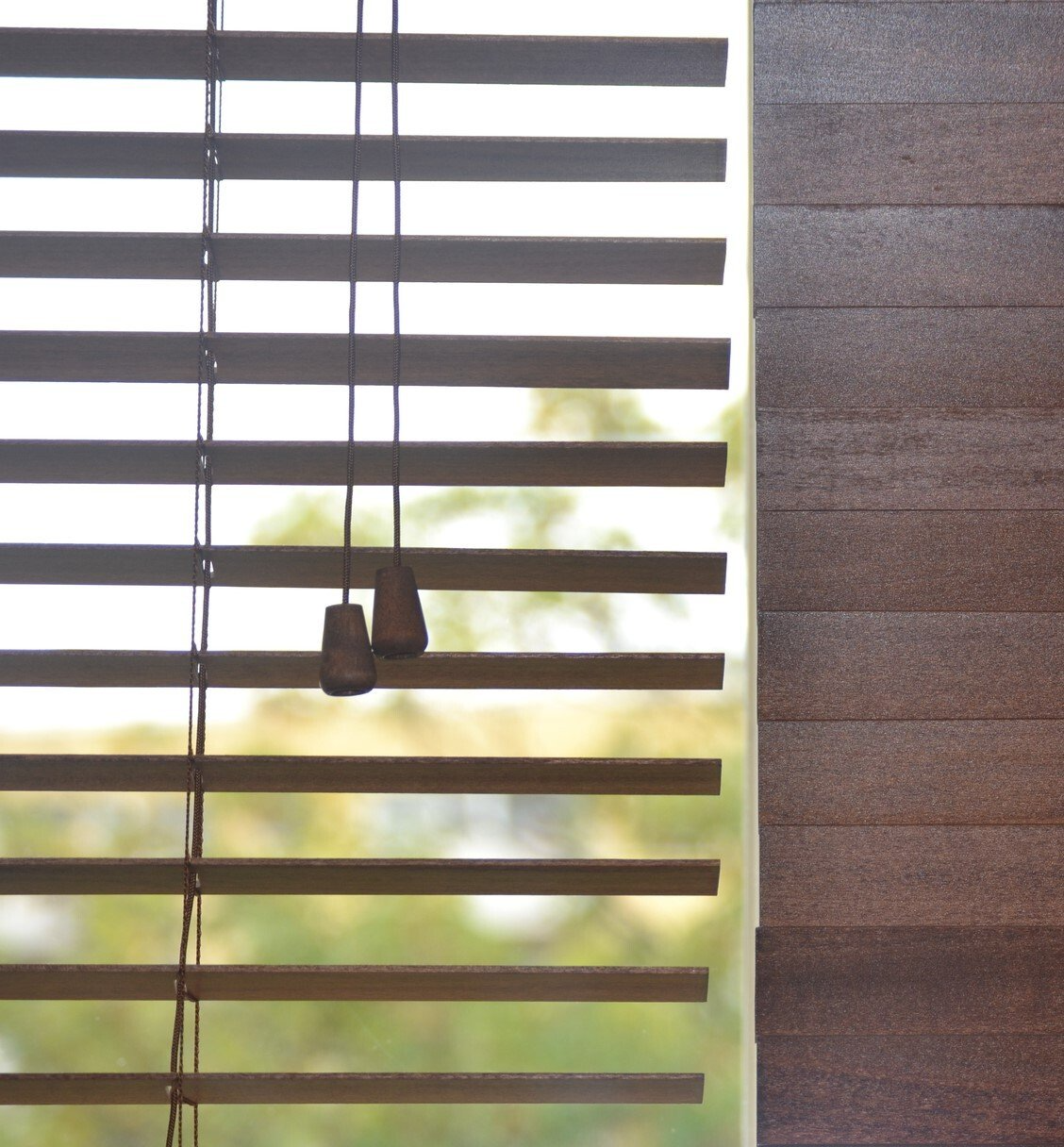 Close up of timber venetions, one side closed and one side open, looking out of trees in the background.