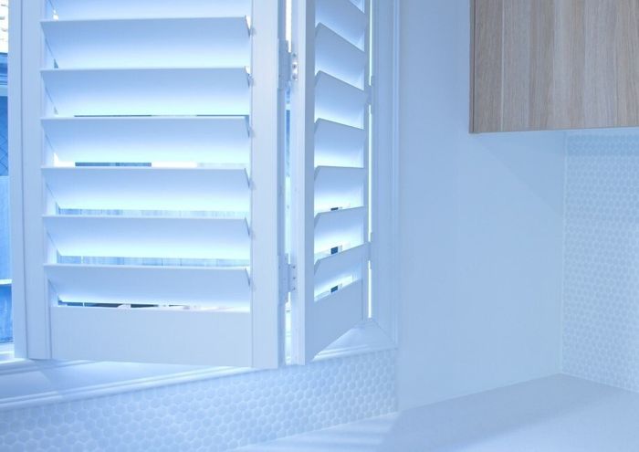 Close up of white french doors pulled open in kitchen, with timber cupboards above.
