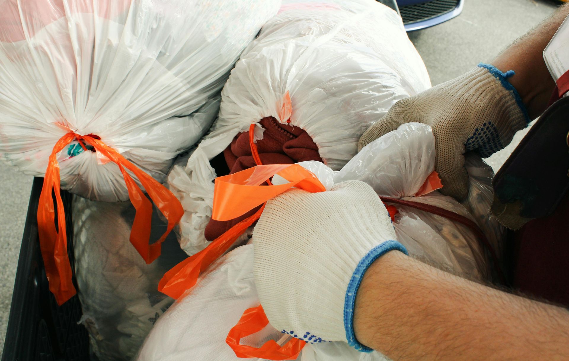 A person wearing gloves is tying a plastic bag with an orange ribbon