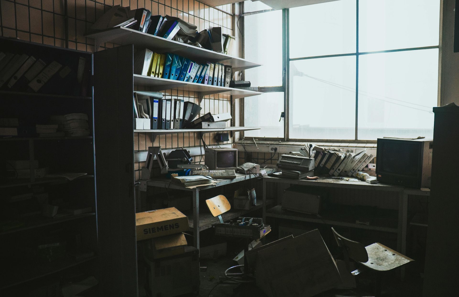 A messy office with a desk , shelves , and a window.