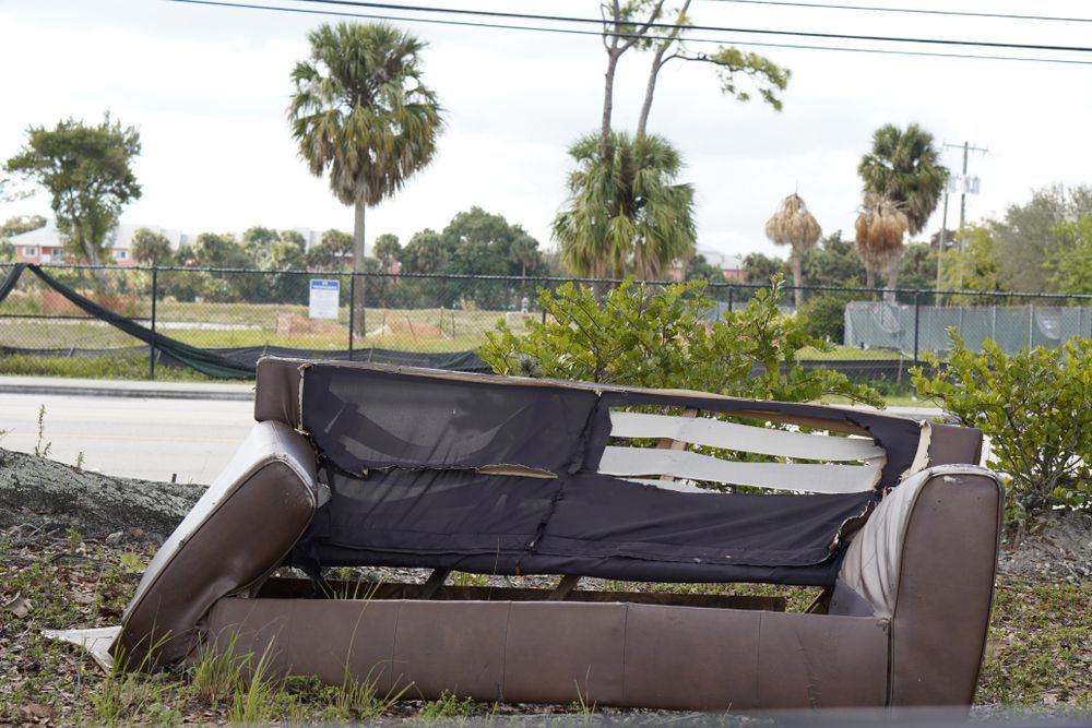 A brown couch is laying in the grass on the side of the road