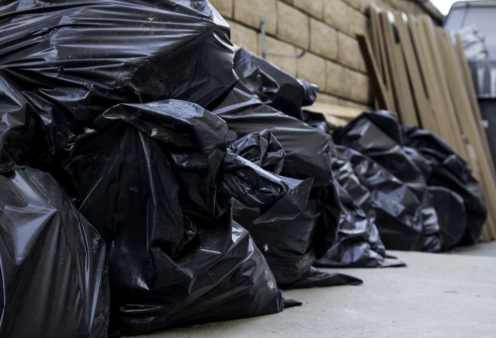 A pile of black garbage bags sitting on the sidewalk in front of a brick wall.
