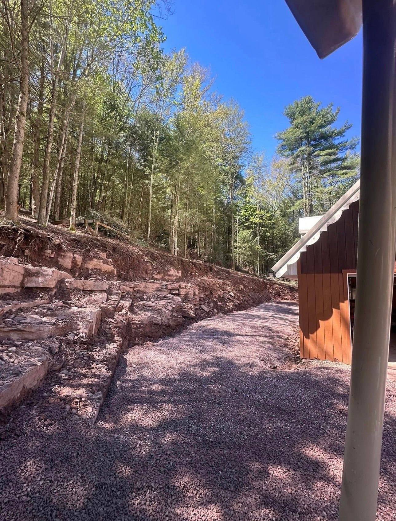 Gravel path beside a wooded hillside and a small cabin under a bright blue sky