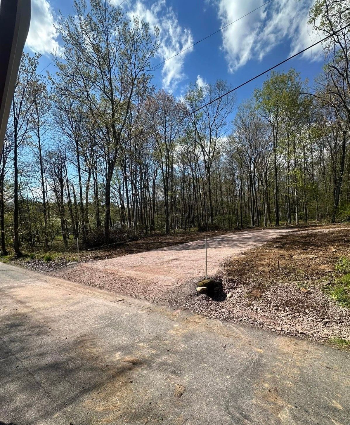 Wooded roadside with a dirt turnout, small drainage culvert, and blue sky overhead