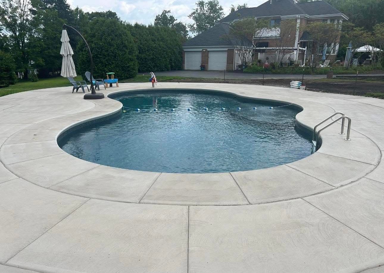 Round backyard swimming pool with concrete deck, ladder, and patio furniture near a house.