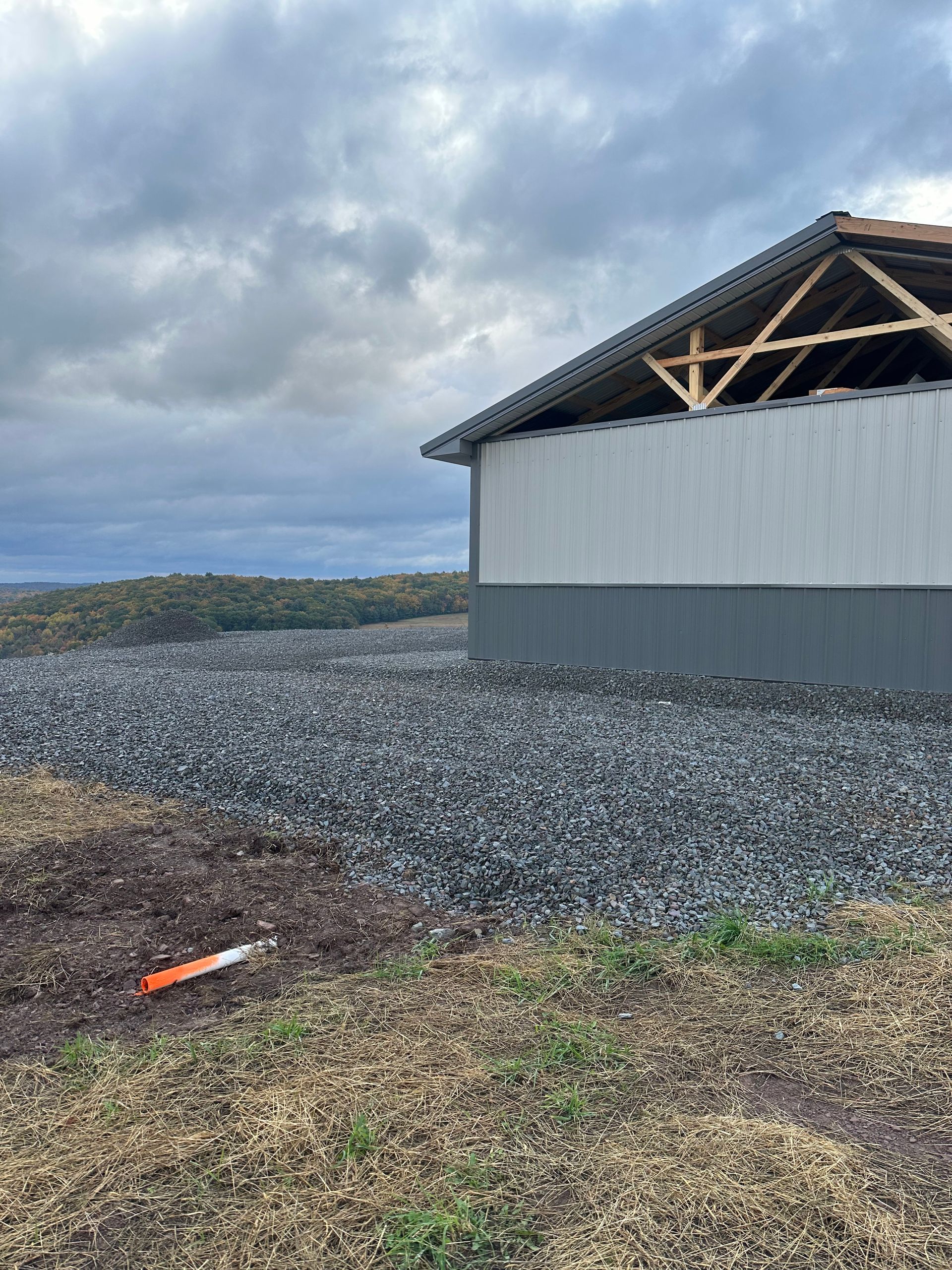 Gravel-covered yard beside a gray building under a cloudy sky, with an orange tool on the ground.