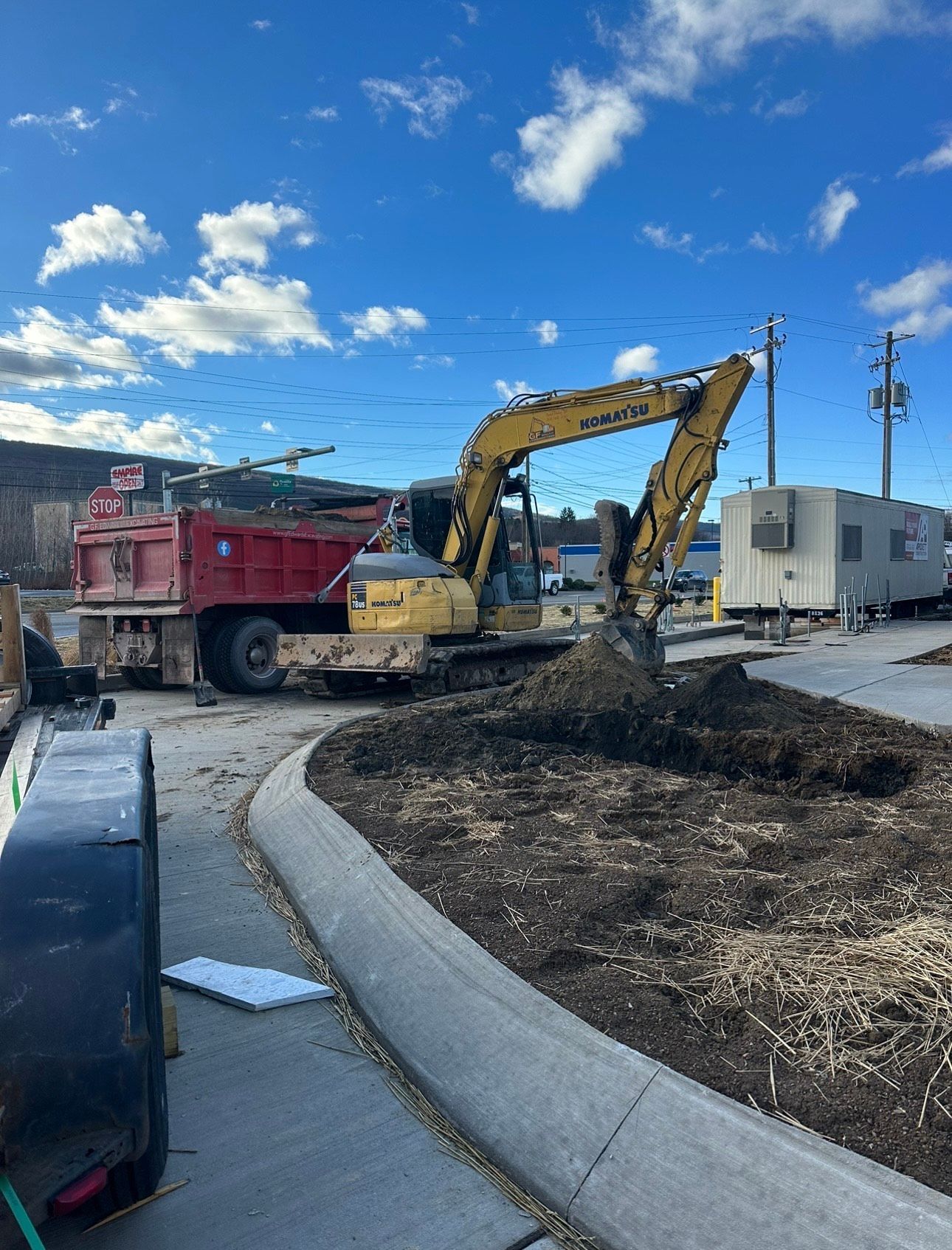 Excavator loading dirt into a red dump truck at a construction site under a blue sky.