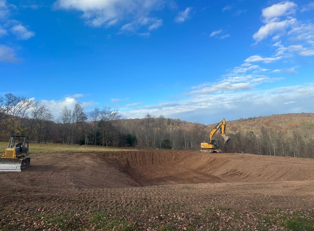Excavators working in a dirt field under a bright blue sky with trees in the background