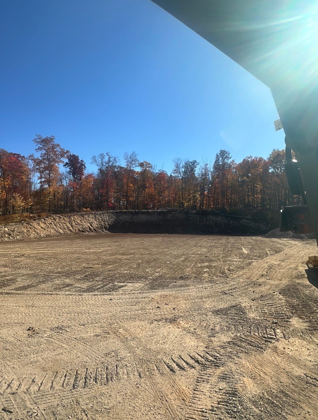 Empty dirt lot beside a tree line under a clear blue sky, viewed from under a roof edge.