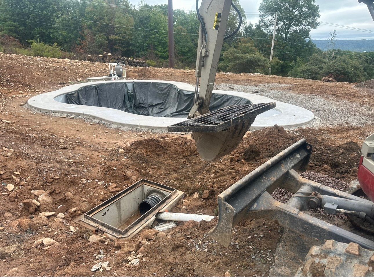 Excavation site with a circular concrete pit, exposed tree trunk, and scattered construction debris on dirt ground