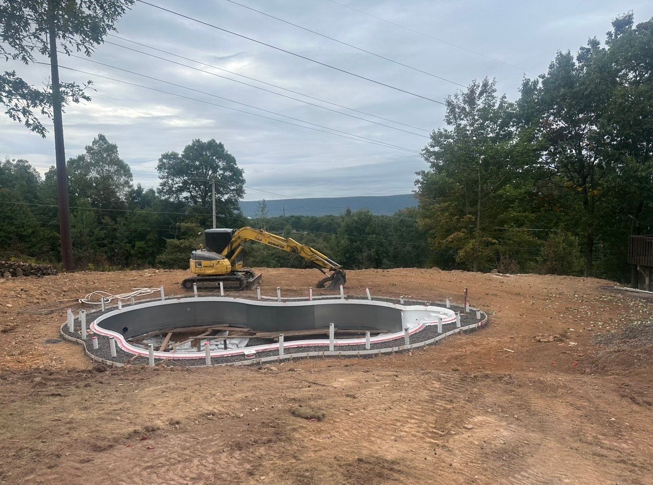 Construction site with excavator digging a circular concrete pit in a wooded clearing