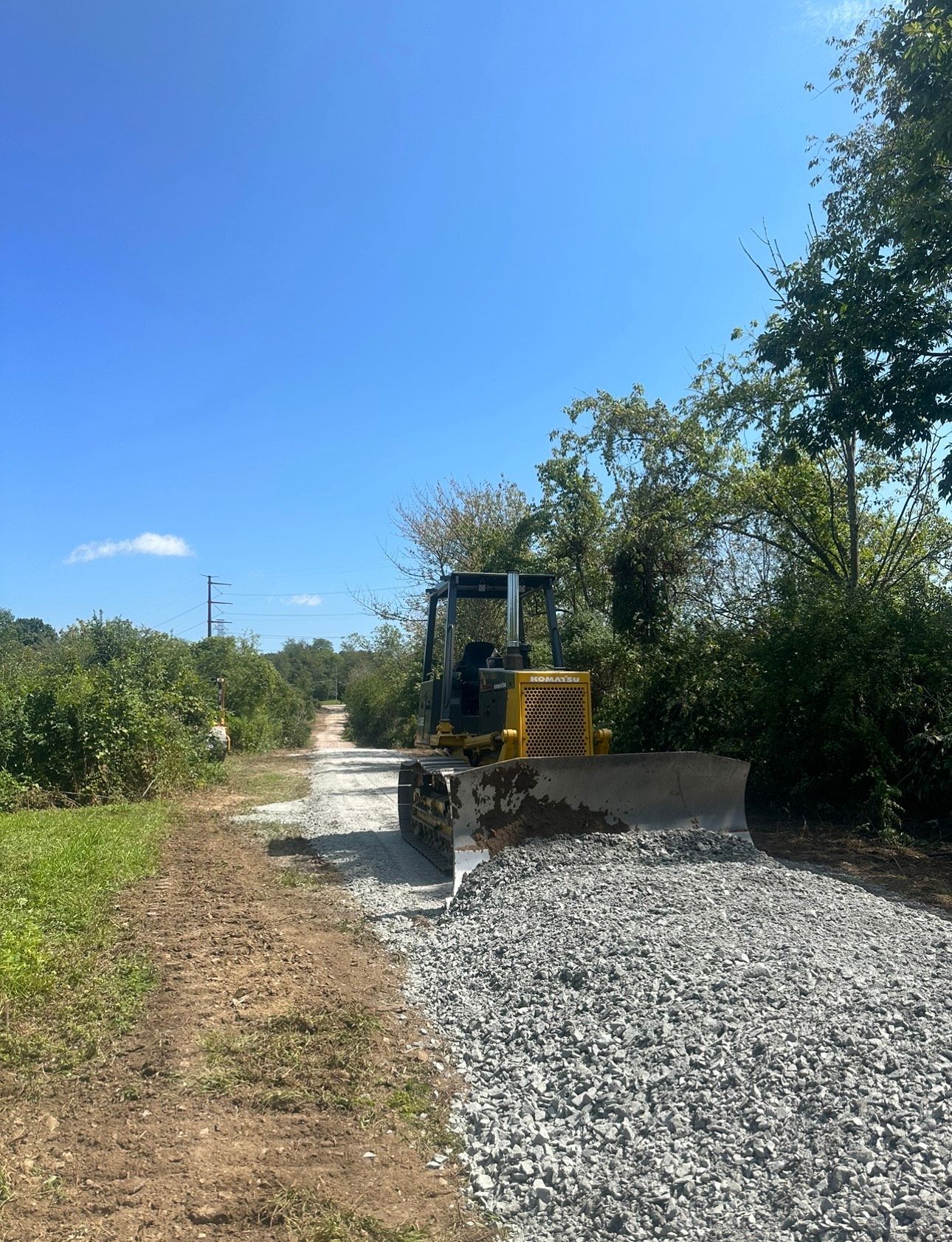 Gravel path beside a small bulldozer and concrete barrier under a clear blue sky