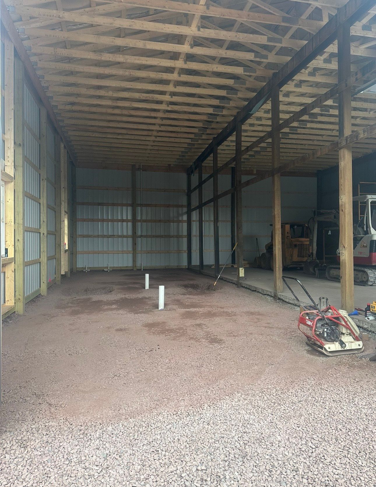 Empty metal warehouse interior with gravel floor, support posts, and construction equipment.