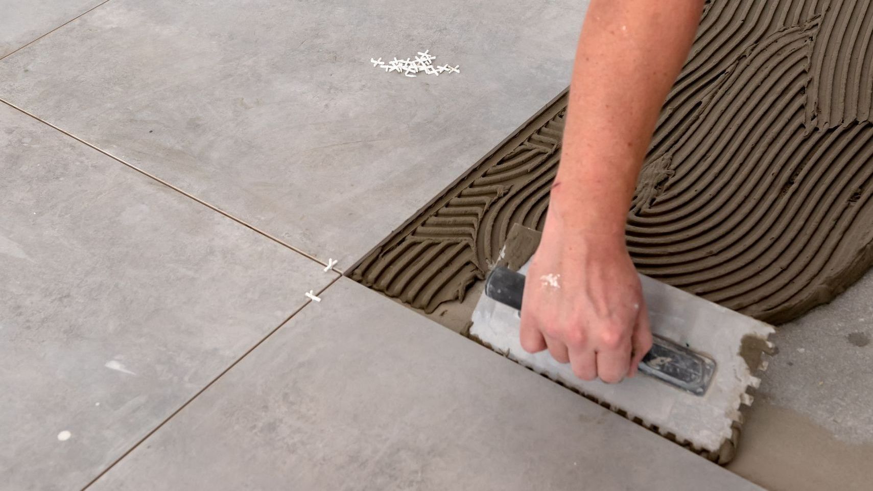 A person is laying tiles on a floor with a trowel.