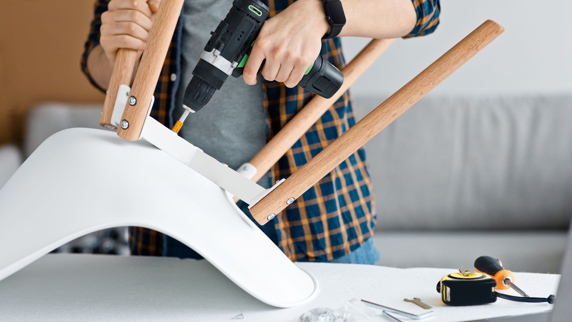 A man is using a drill to fix a chair.