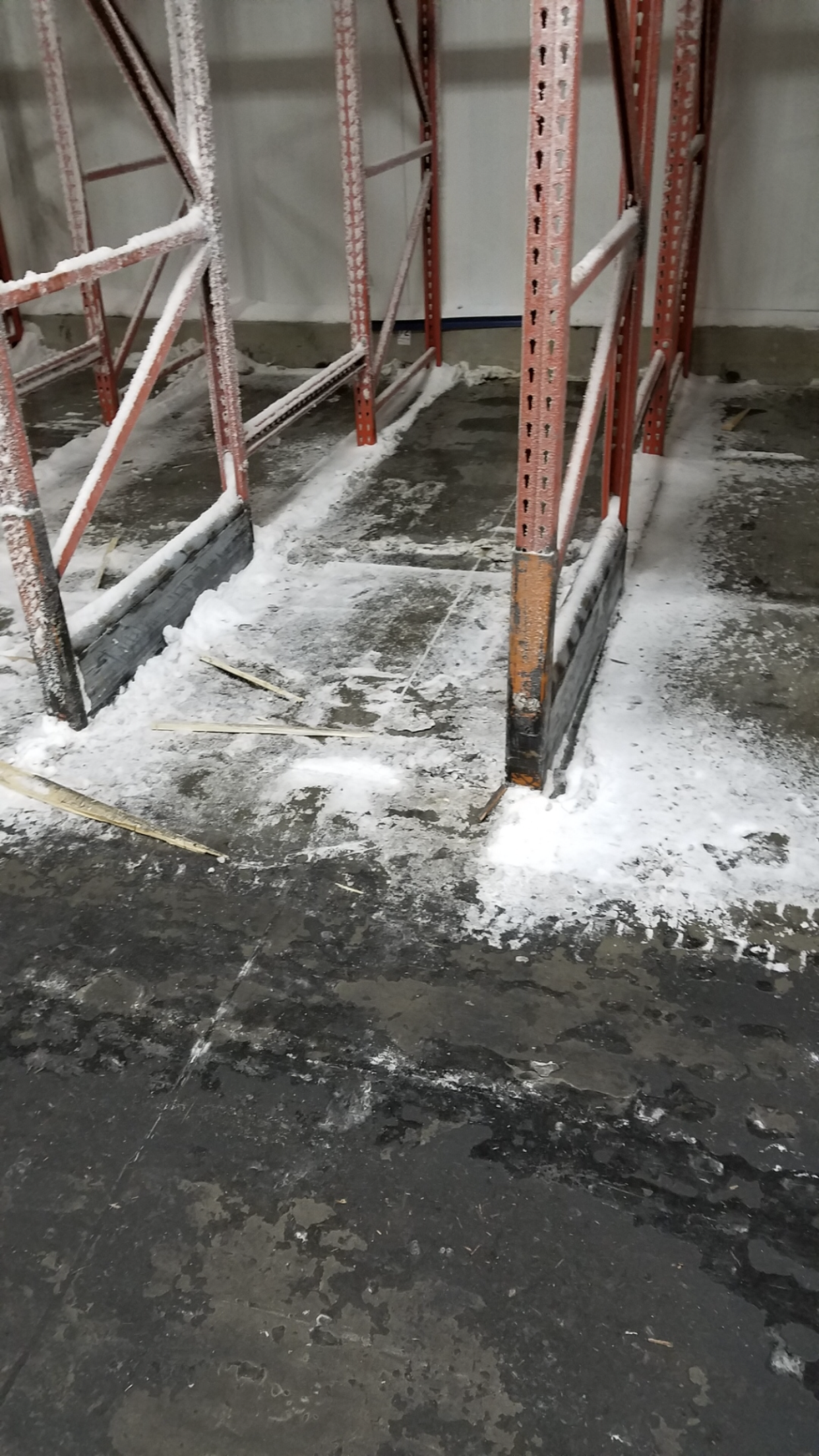 Warehouse floor, industrial shelving covered in white substance, floor appears wet and stained.