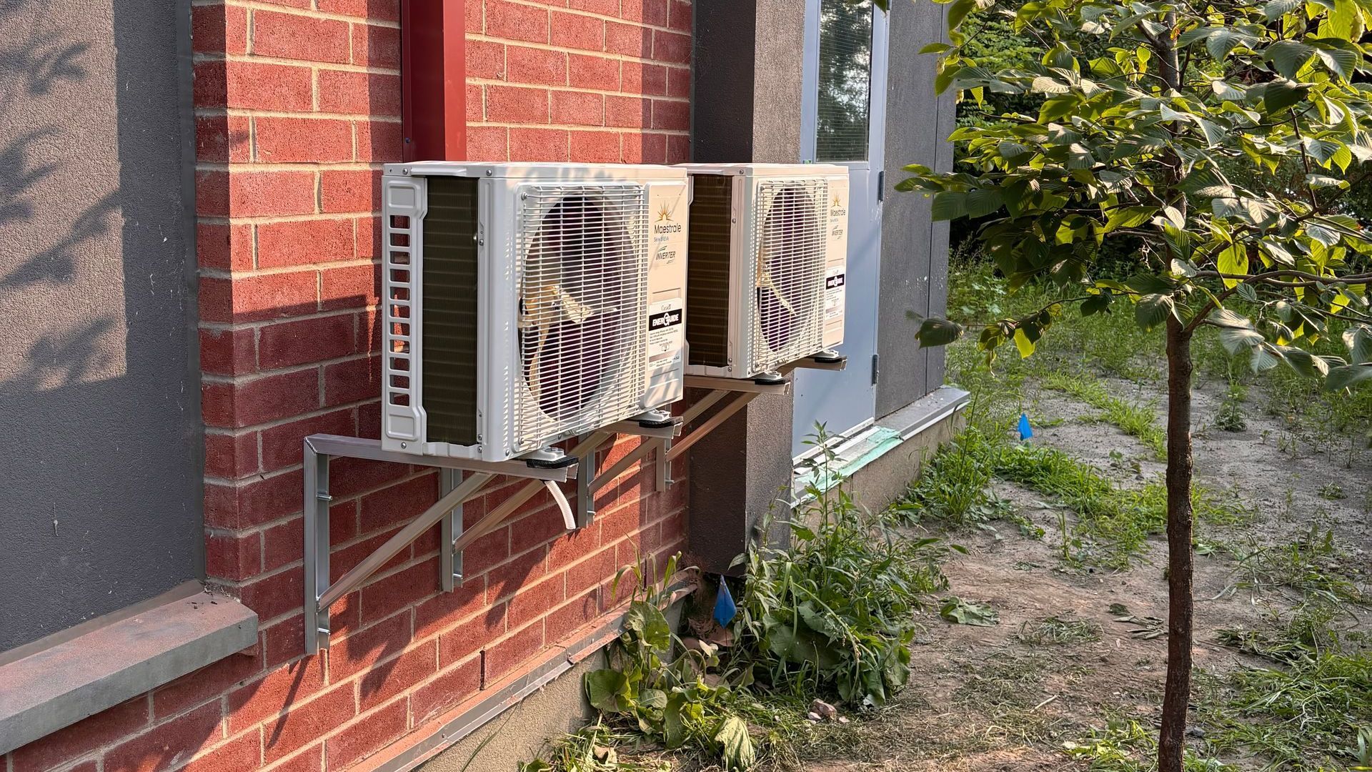 Deux unités de climatisation blanches fixées sur la façade d'un bâtiment en briques et en stuc.