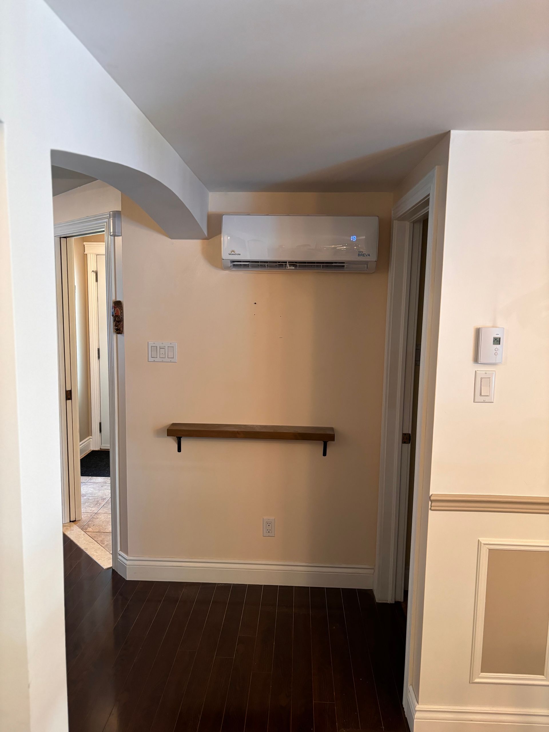Wall-mounted air conditioner installed in a room with beige walls and dark flooring.