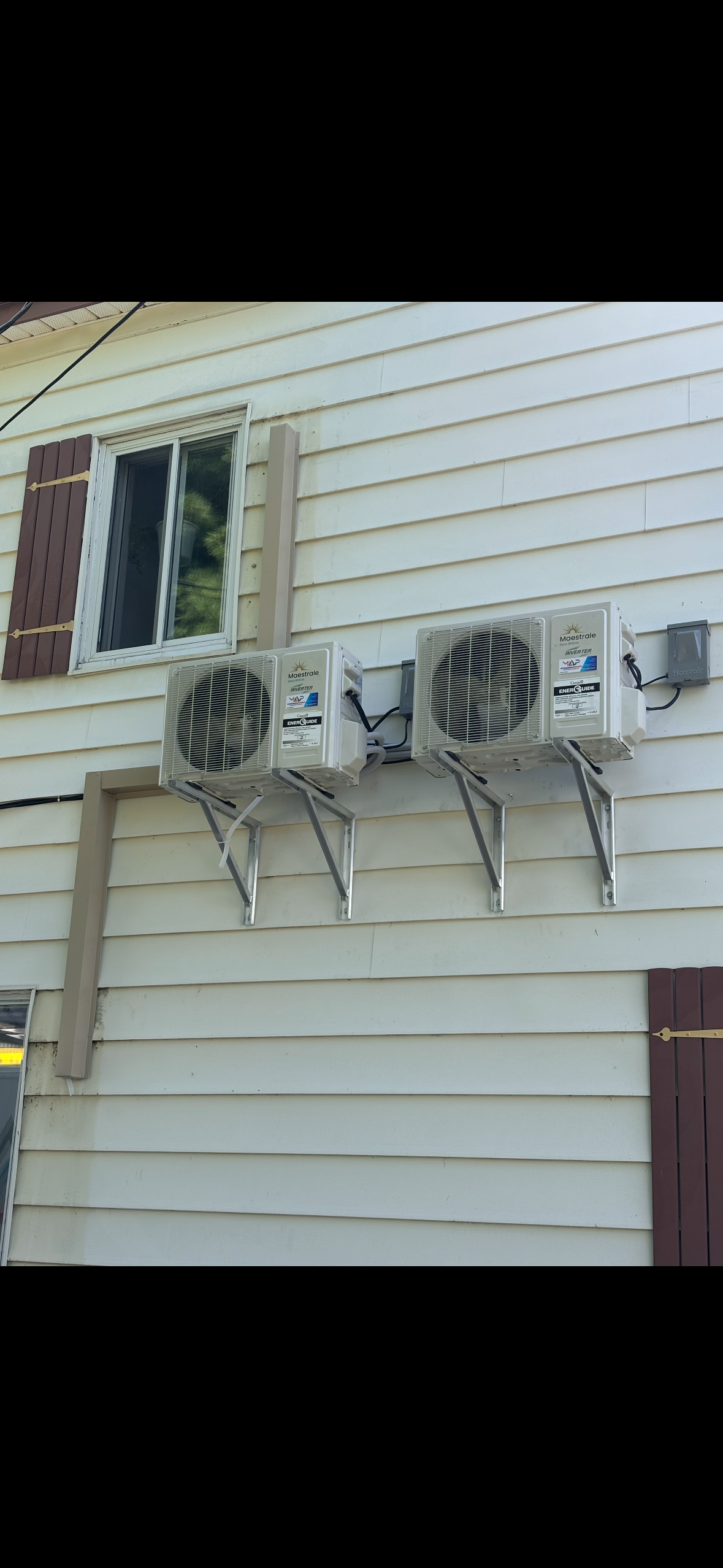 Trois unités de climatisation murales fixées à une maison au revêtement blanc.