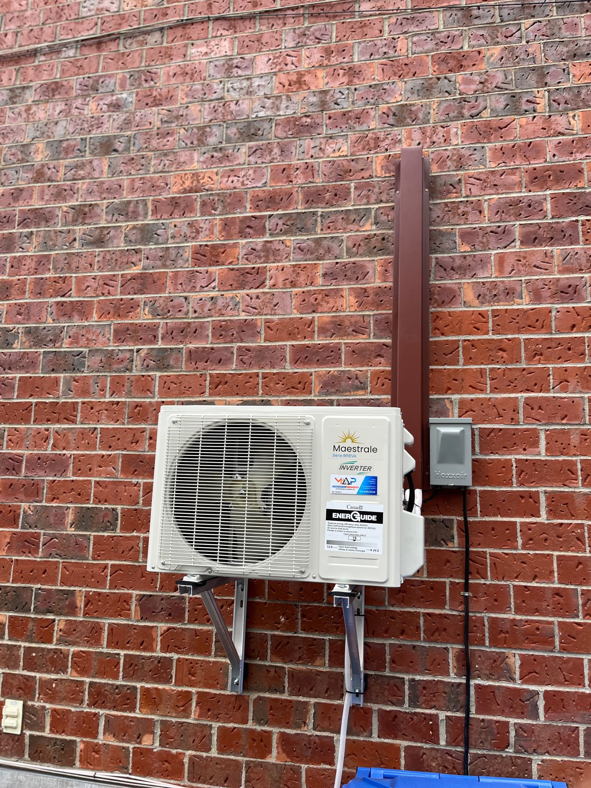 Unité de climatisation fixée à un mur de briques avec un conduit électrique.