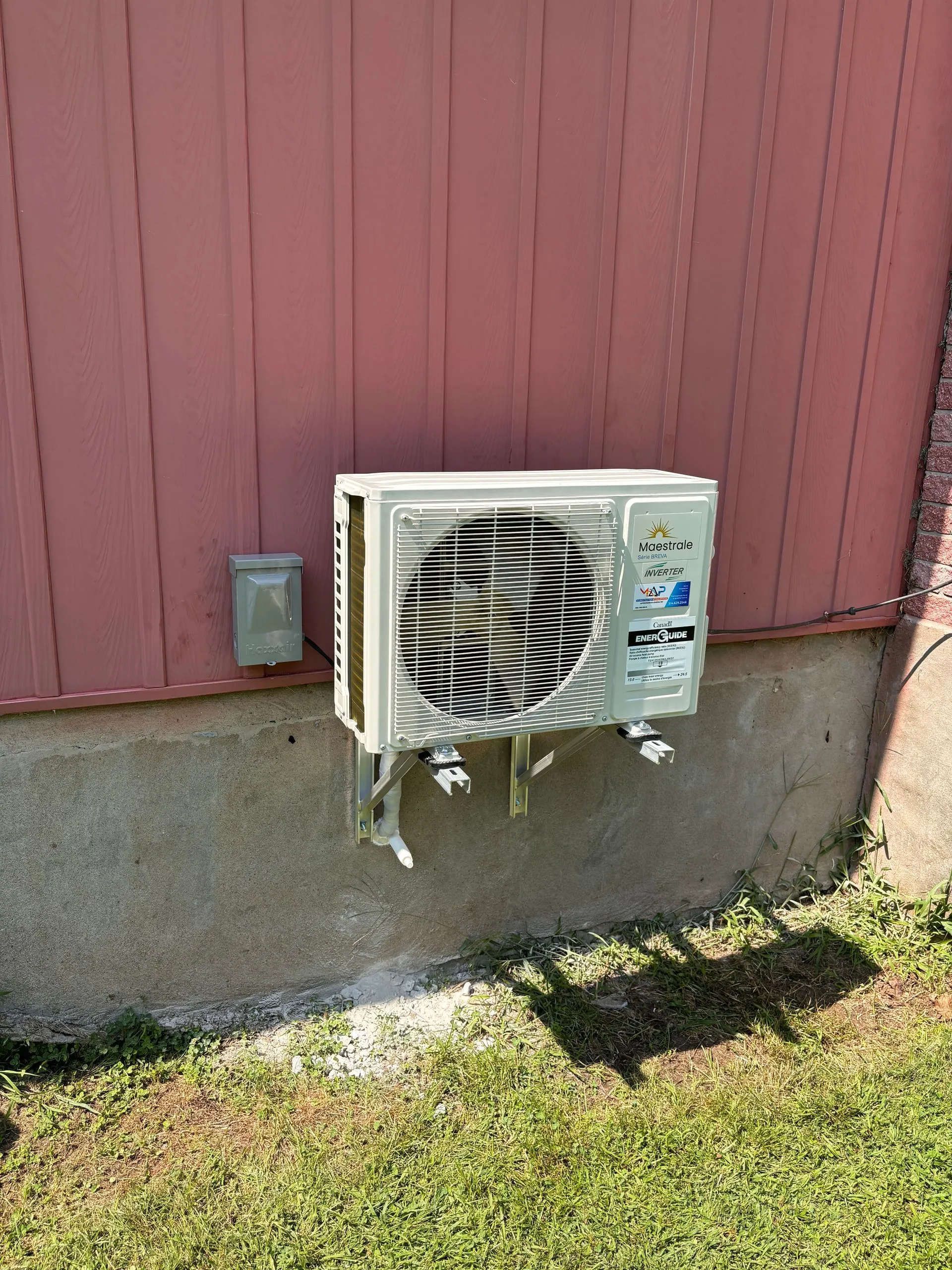 Unité extérieure de climatiseur installée sur support métallique contre un mur rouge.