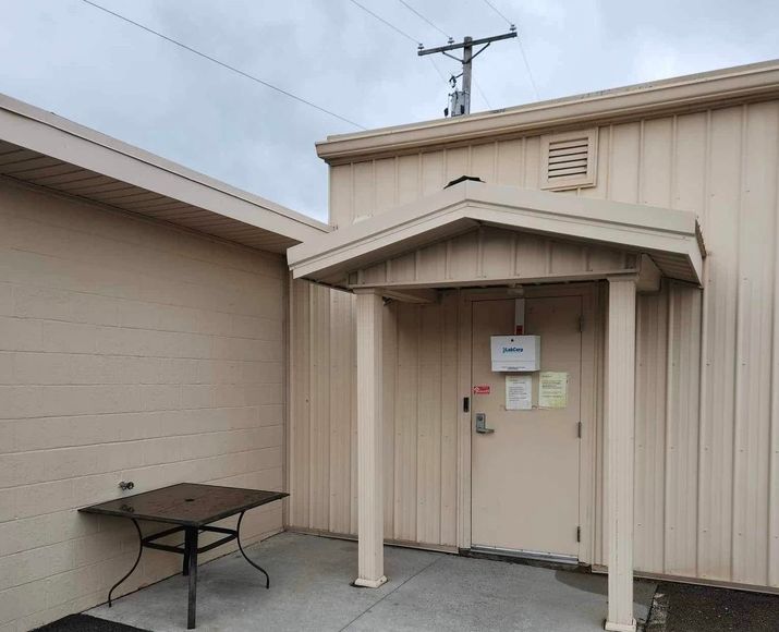 Beige utility building entrance with awning, posted signs, and a small table beside it