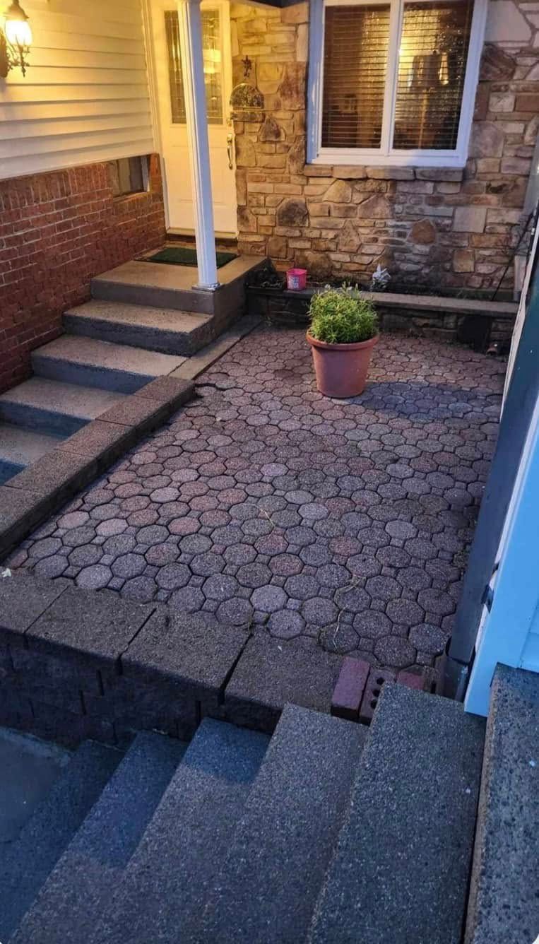 Brick and stone front entry patio with steps, potted plants, and a window by the house