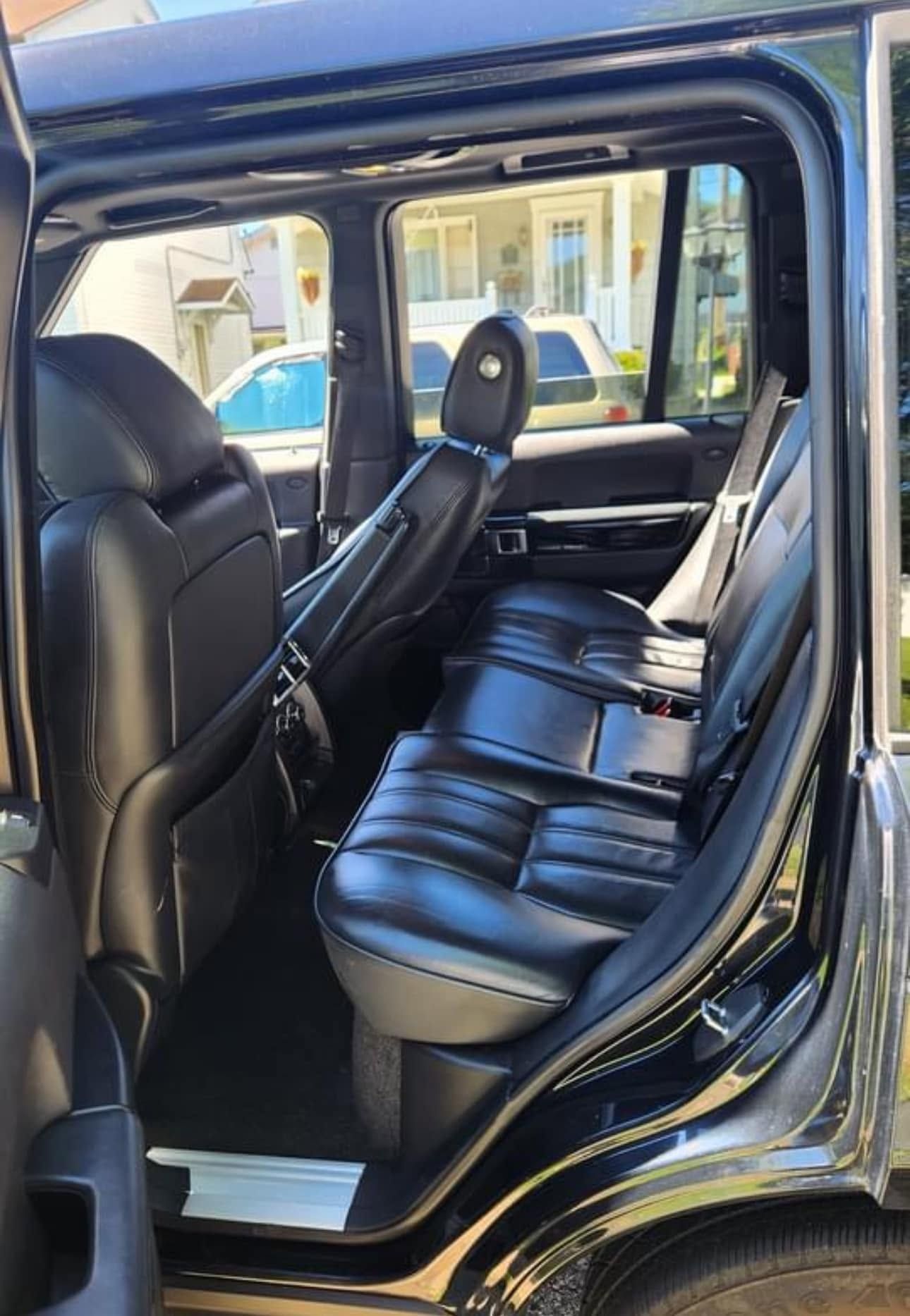 Black leather back seat of a vehicle with the door open, showing three-seat bench and front seat back.